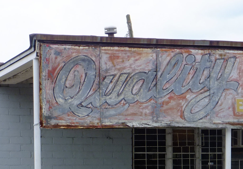 Photograph of faded sign on building front showing the word 'Quality'.